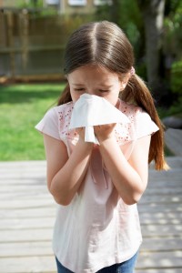 Young girl sneezing into a white tissue.
