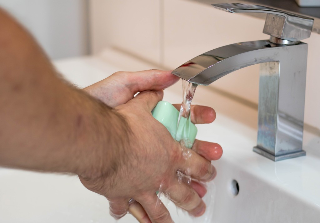 Image shows a close up of a pair of hands washing with soap in a sink.