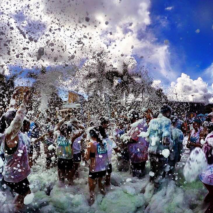 Group shot of runners in a race dancing in a foam party at the finish line